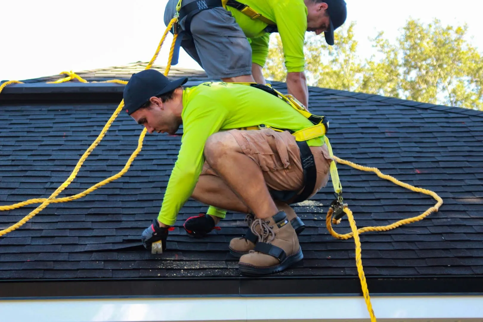 Two roofers with tethers repairing shingle roof